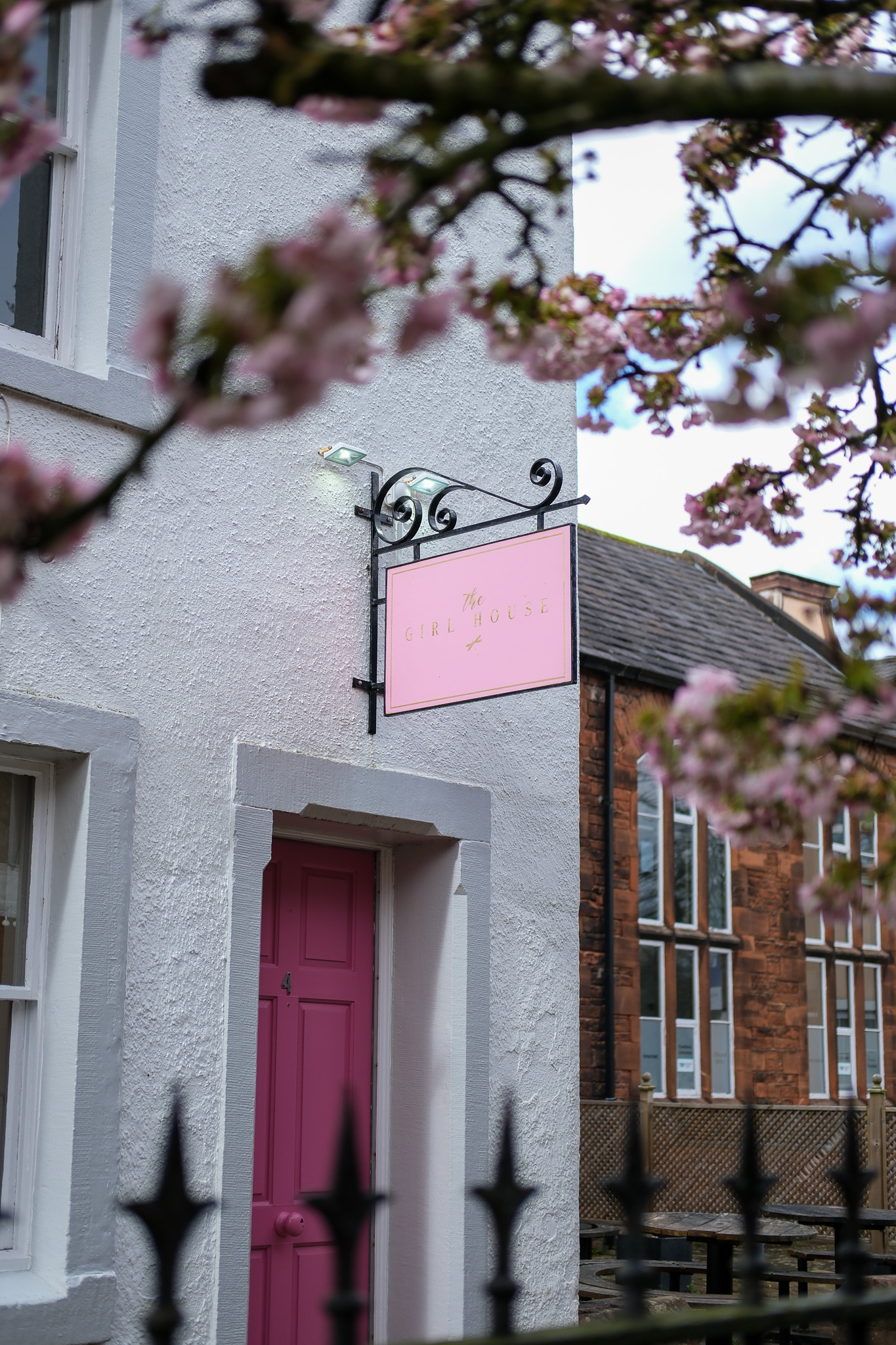 The white salon building with its pink front door and hanging sign