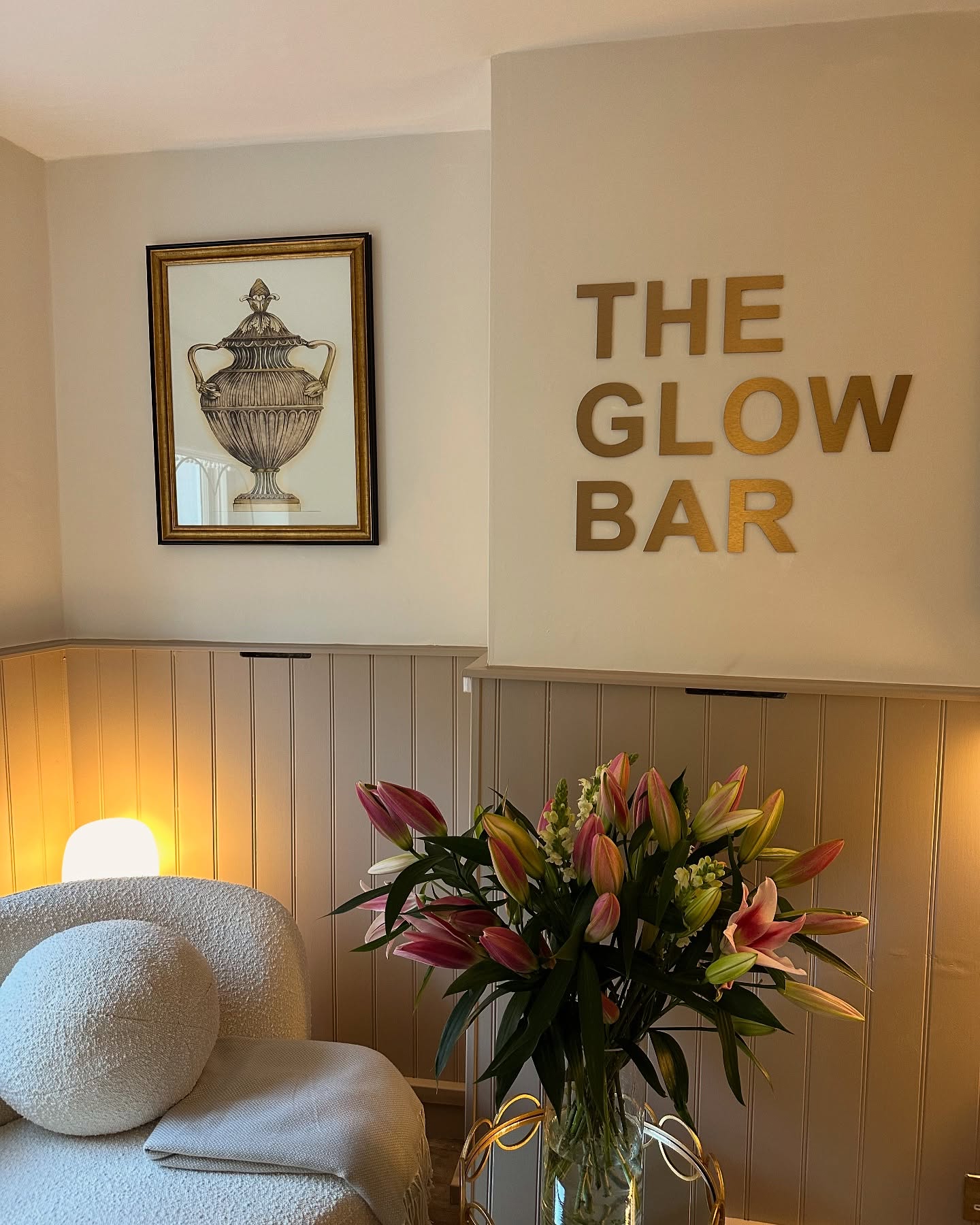 The Glow Bar treatment room with a gold sign, lamp and lilies